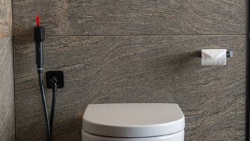 A modern bathroom with a toilet, a paper towel dispenser, and a black electrical outlet.