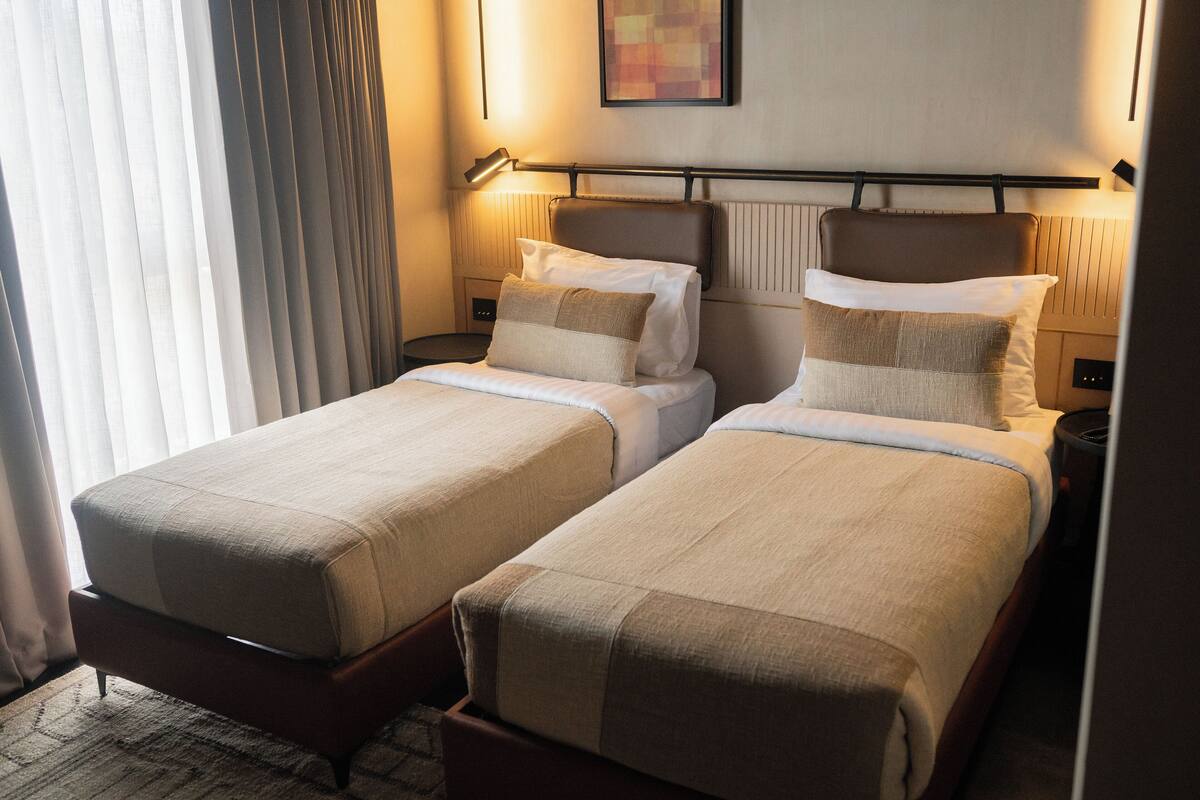 Une chambre d’hôtel avec deux lits simples, chacun comprenant un oreiller et une couverture, une table de chevet et une lampe.