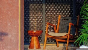 A wooden chair with a woven seat and backrest, a small wooden table, and a potted plant. - TERRATONE BOUTIQUE BUSINESS HOTEL (Kollam)