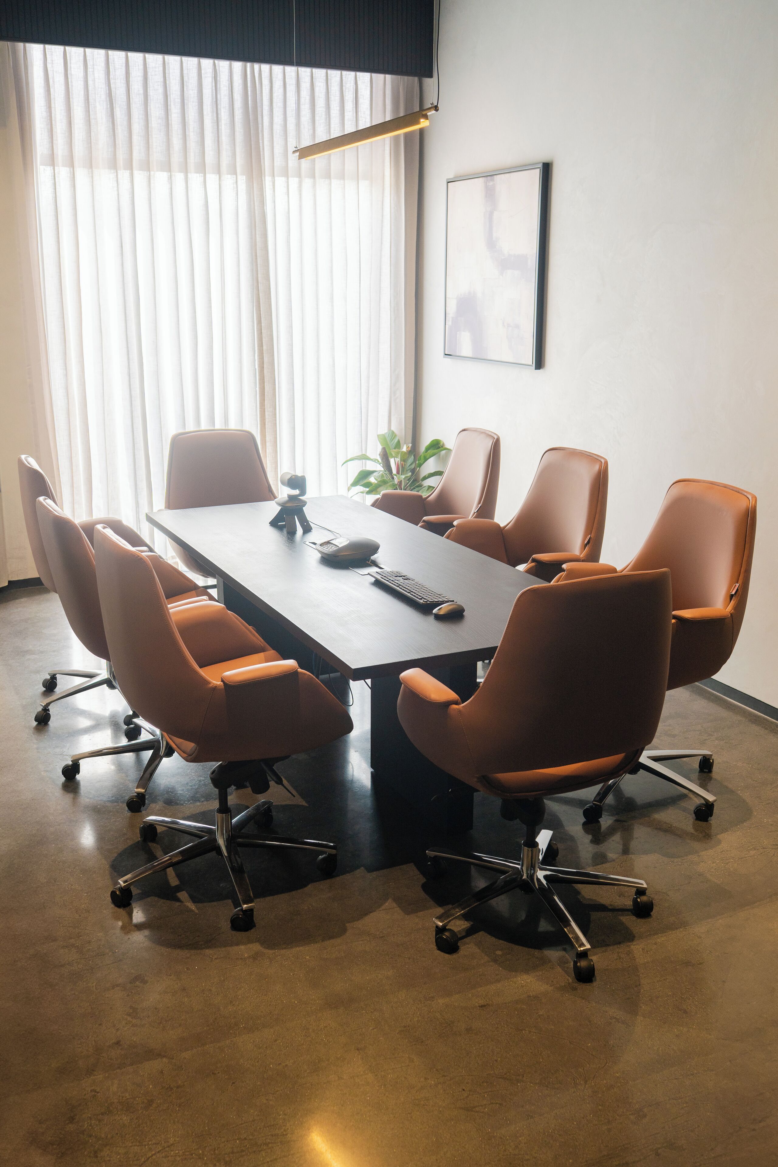 Une salle de conférence avec une longue table, six chaises, une plante et un tableau encadré au mur.