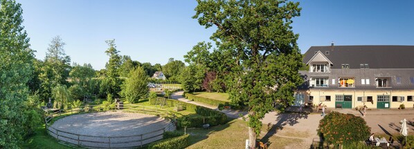 A large building with multiple windows and a balcony, surrounded by well-maintained gardens and a circular gravel area.