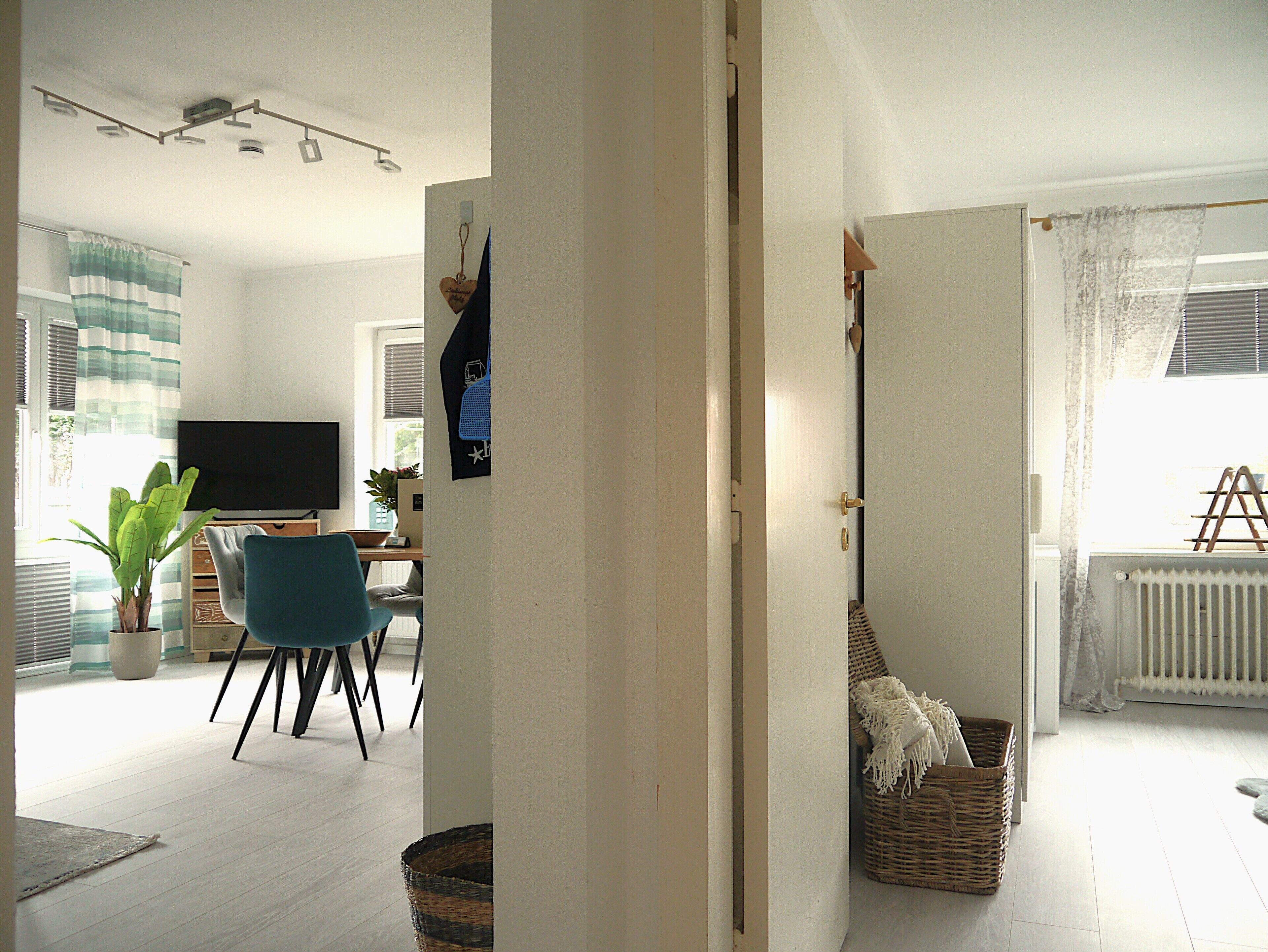 Un salon avec un téléviseur, un fauteuil bleu, une plante et un panier en osier.