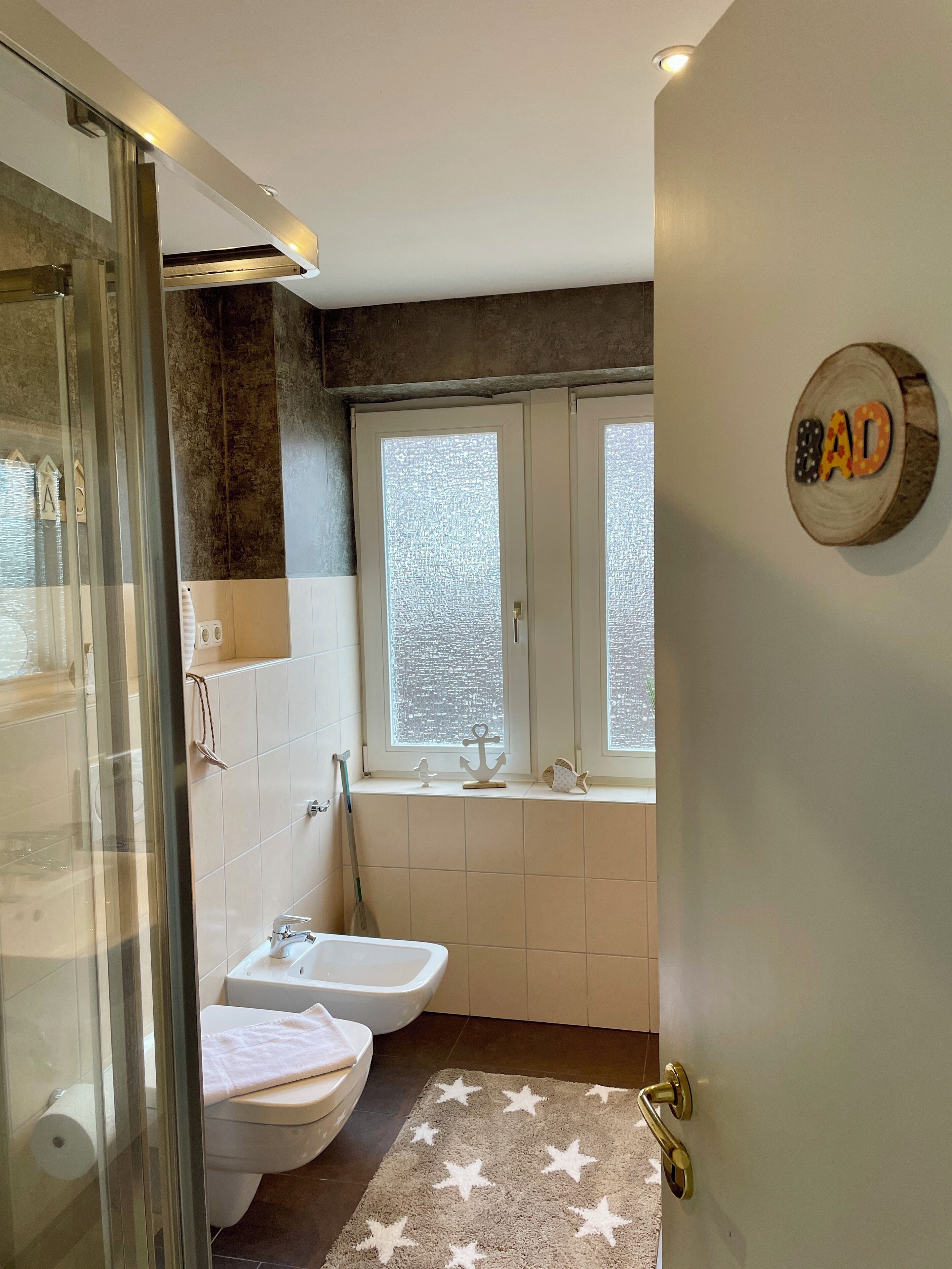 A bathroom with a shower, toilet, bidet, and a window with a view of trees.