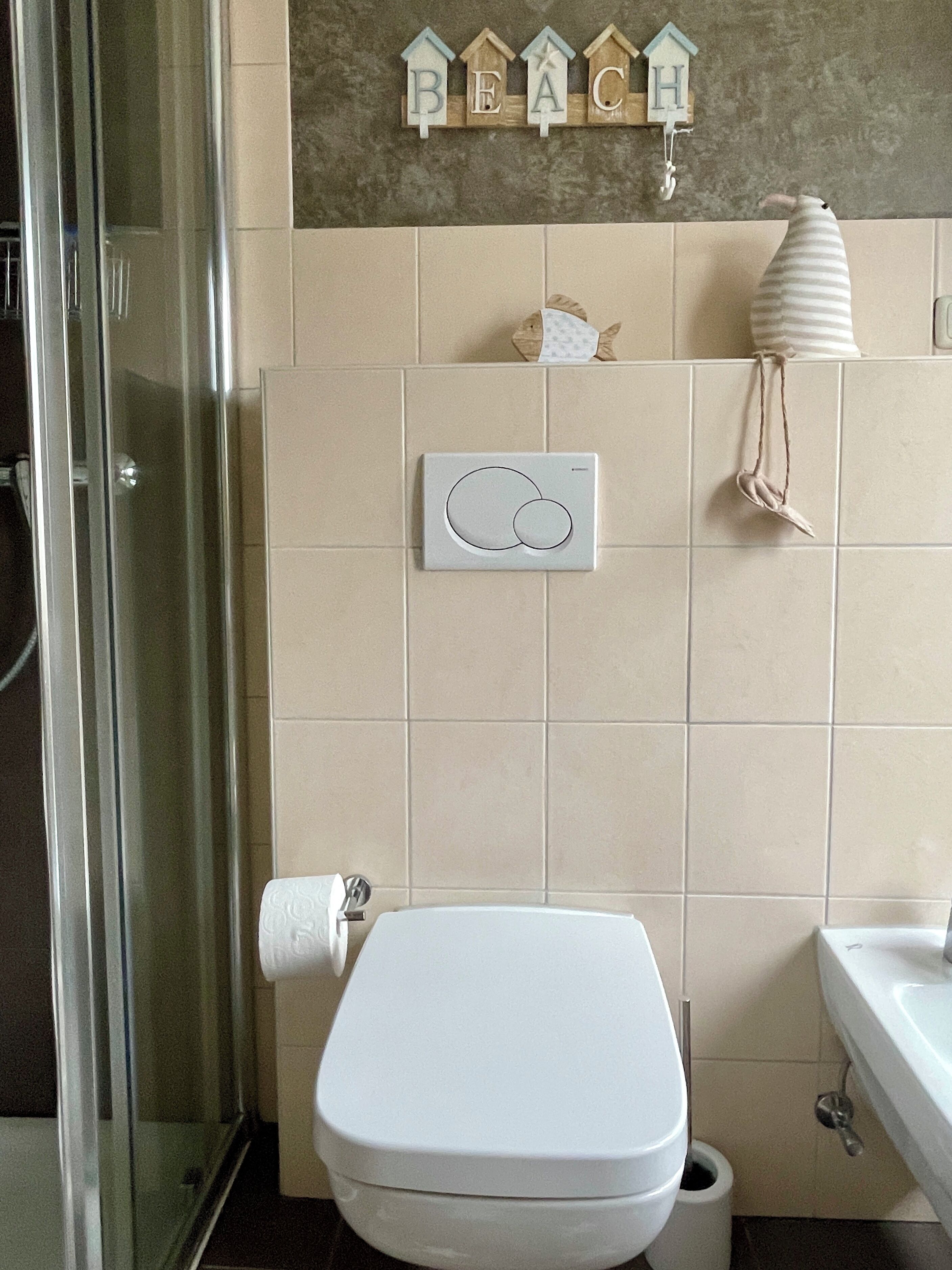 Une salle de bain équipée de toilettes, d’une douche et d’un lavabo. On y trouve un porte-serviettes avec une serviette, ainsi qu’un panneau décoratif au-dessus des toilettes.