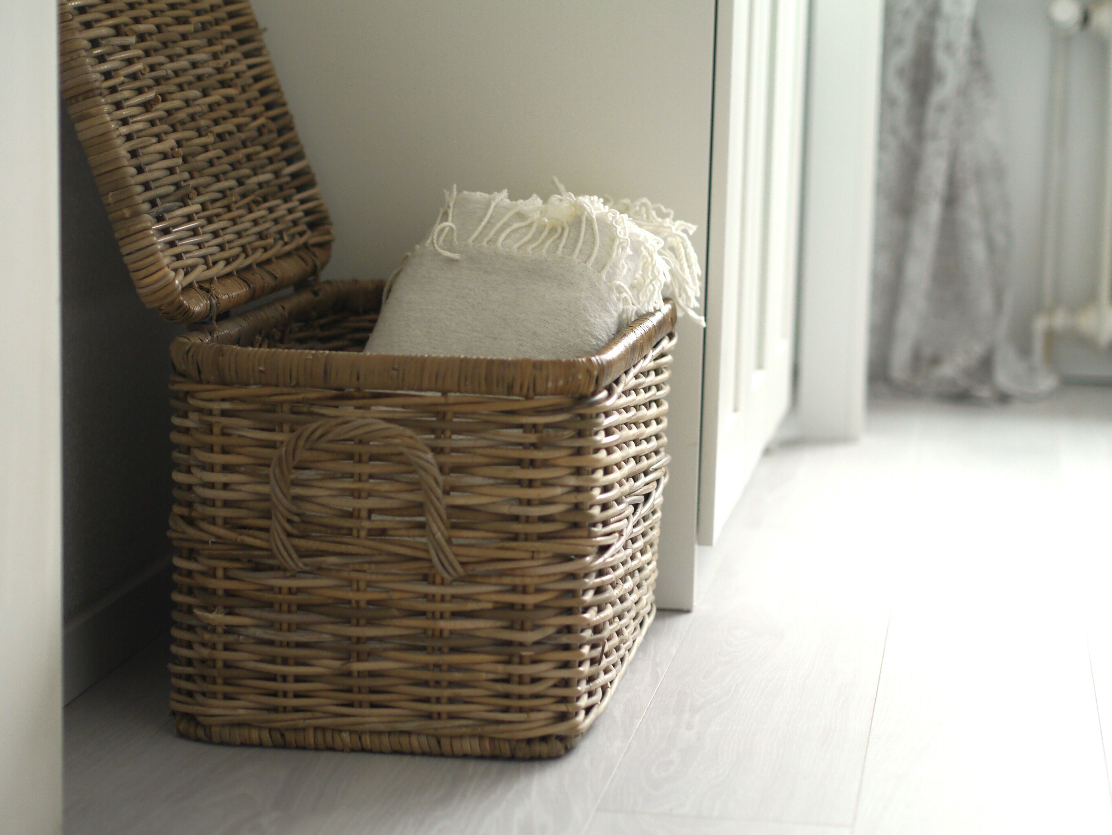 A wicker basket with a white cushion, placed against a wall near a window.