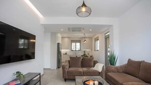Una sala moderna con televisor de pantalla plana, sofás, una mesa de centro con velas y una cocina al fondo.