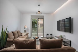 Un salon moderne avec un canapé, une table basse, un lampadaire, un téléviseur fixé au mur et une vue à travers une porte vitrée.