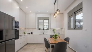 Una cocina moderna con armarios blancos, una mesa de comedor con sillas, un refrigerador e iluminación colgante.