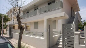 Un edificio moderno de dos pisos con entrada porticada, una escalera y un árbol en primer plano.