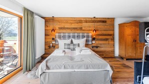 A modern bedroom with a wooden headboard, a large bed with white bedding, a view of the outdoors through a large window, and a wooden wardrobe. - Studio Winklmoos | Pool, sauna & mountain view (Reit im Winkl)
