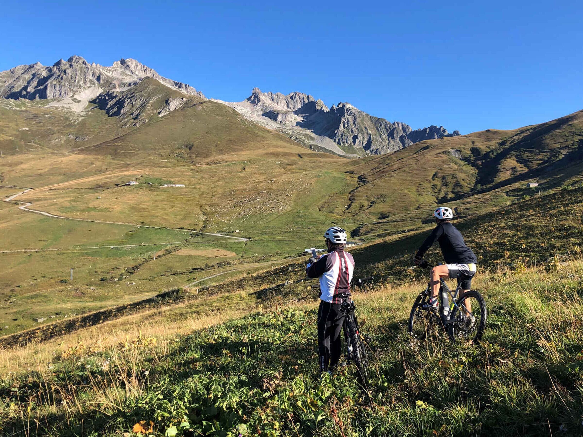 A mountainous landscape with two cyclists on a trail.