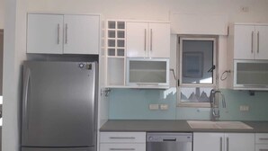Cocina compacta con alacenas blancas, un refrigerador de acero inoxidable, lavavajillas y ventana con vista a la montaña.
