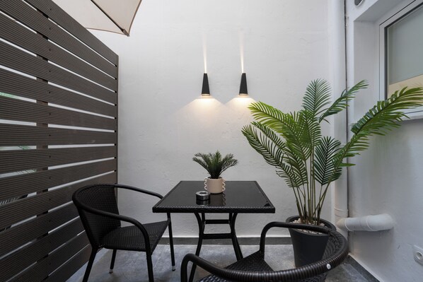 Un pequeño espacio al aire libre con una mesa y dos sillas, una planta en maceta y dos luces fijadas a la pared.