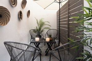 Un patio con dos mesas, cuatro sillas, una planta en maceta y una pared decorada con detalles tejidos.