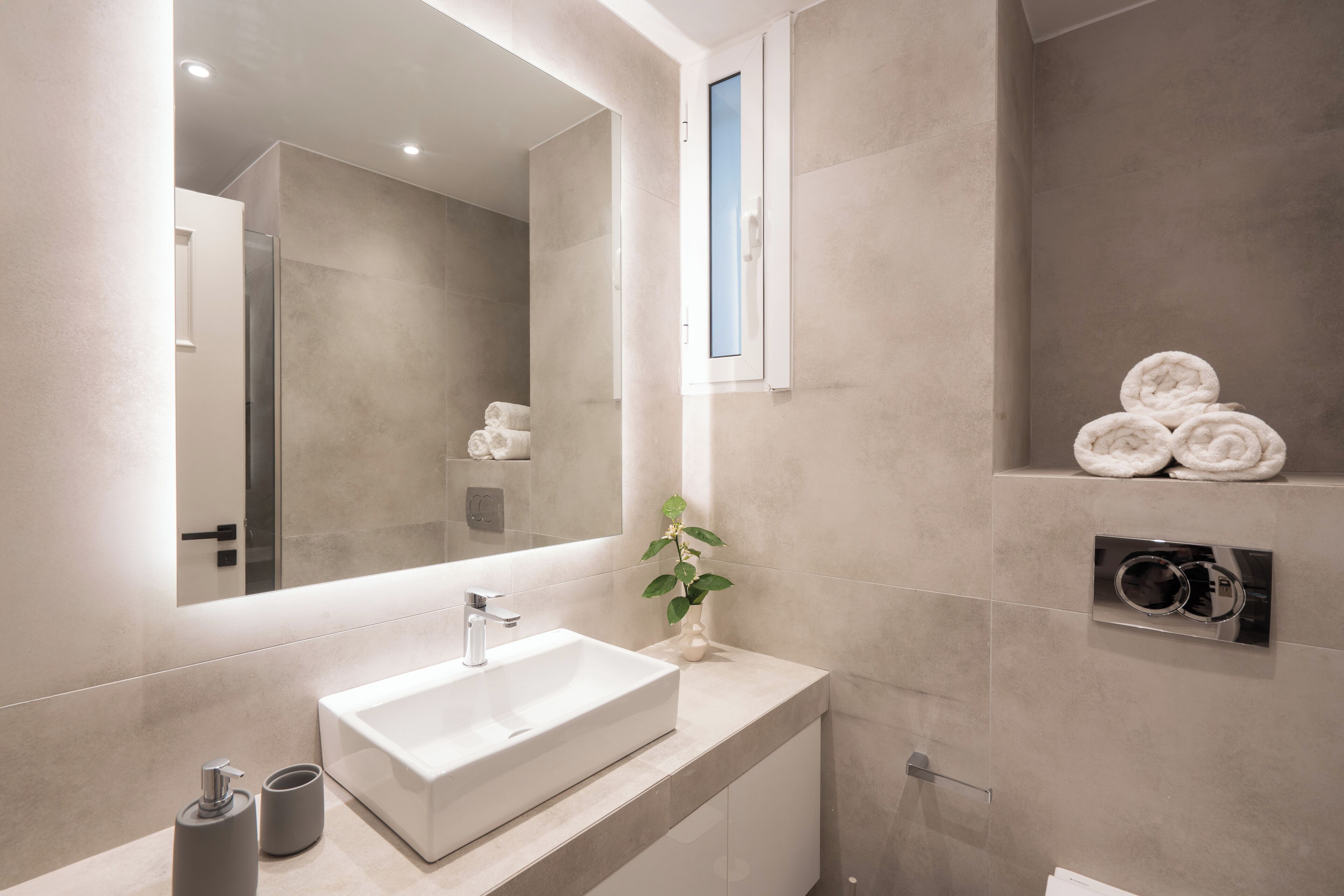 A modern bathroom with a large mirror, a white sink, and a towel rack.