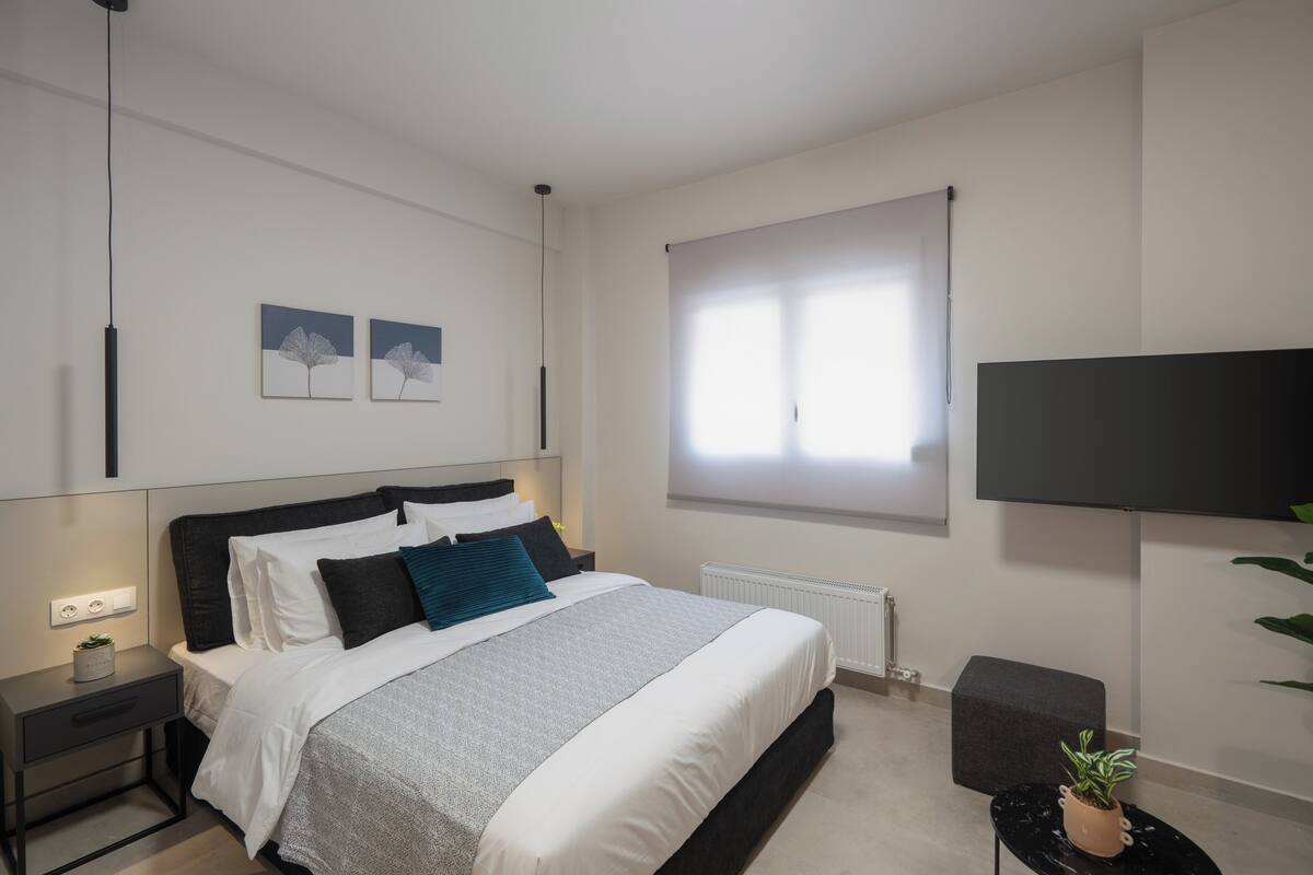 Een moderne slaapkamer met een bed, nachtkastjes, een radiator, een televisie en kunst aan de muur.