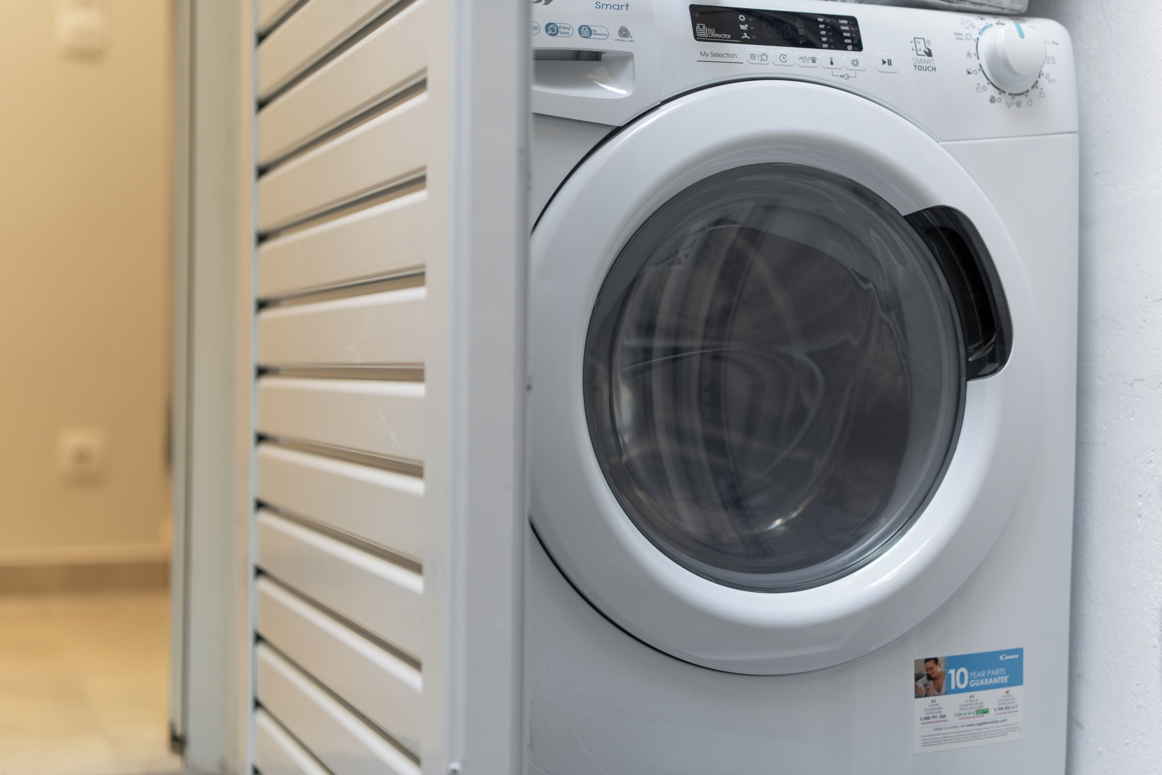A front view of a white washing machine with a digital display and a 10-year parts guarantee sticker.