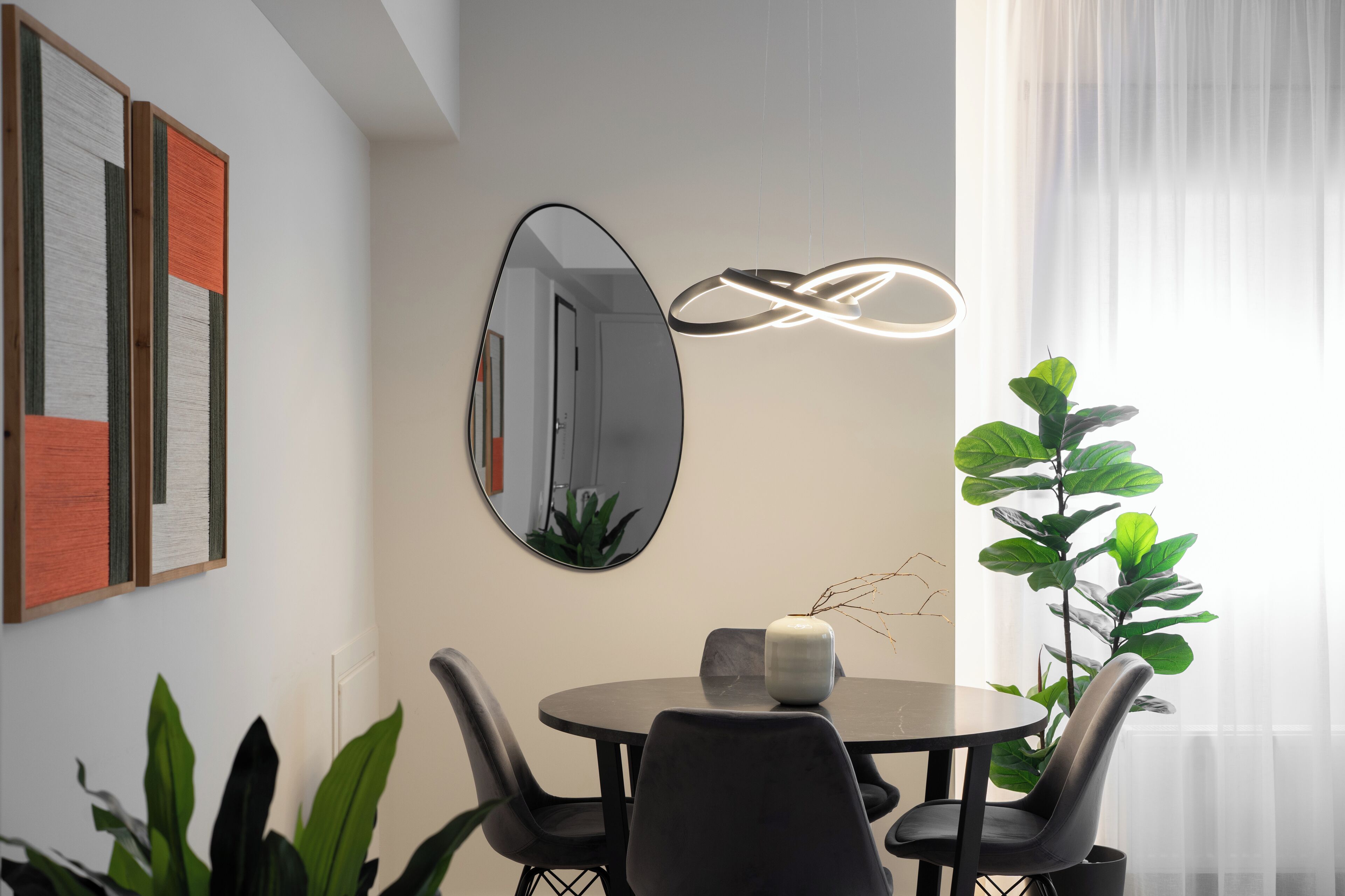 A modern dining area with a round table, black chairs, a white vase, and a large mirror.