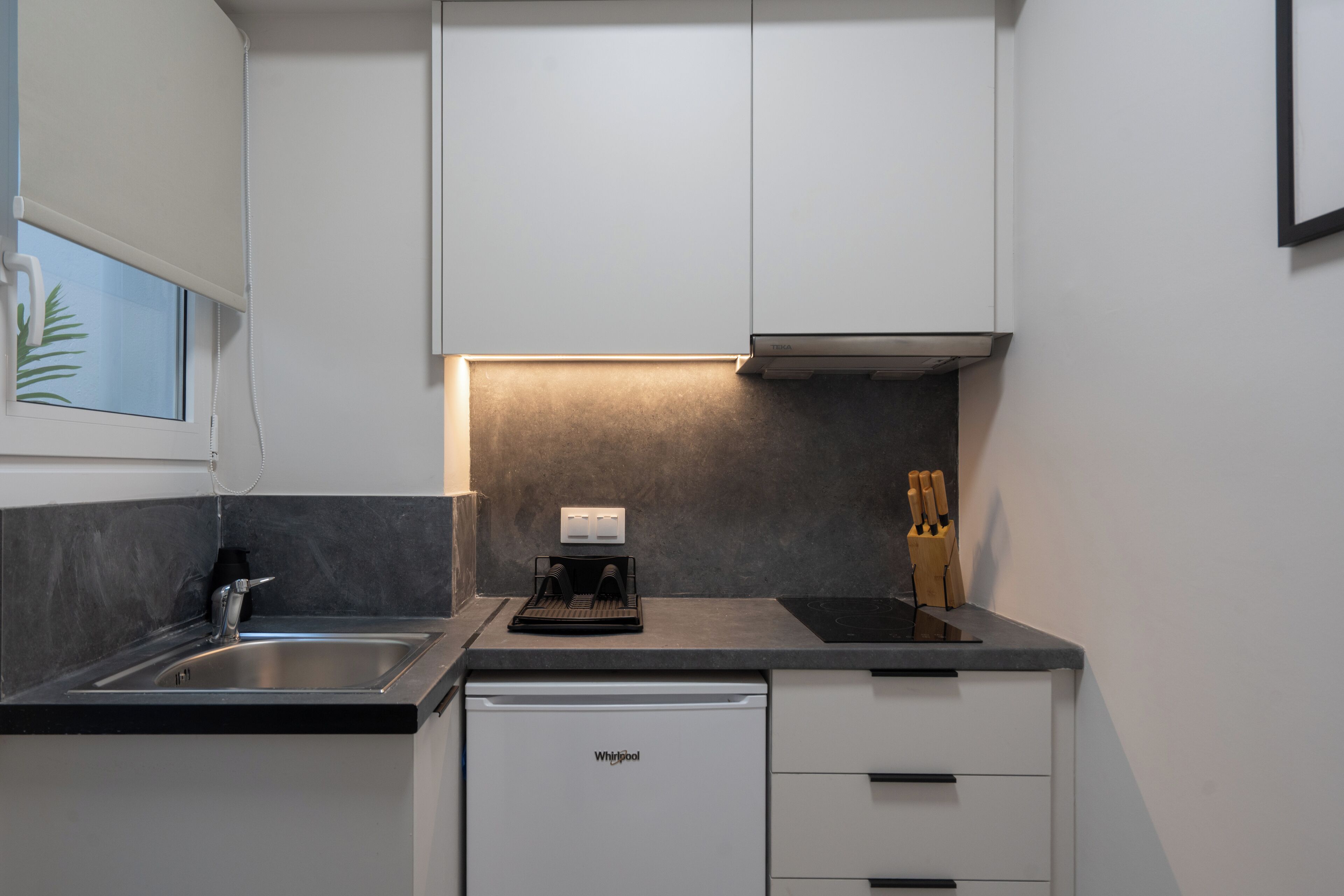 A compact kitchen with a built-in dishwasher, a coffee maker, and a knife block on the countertop.