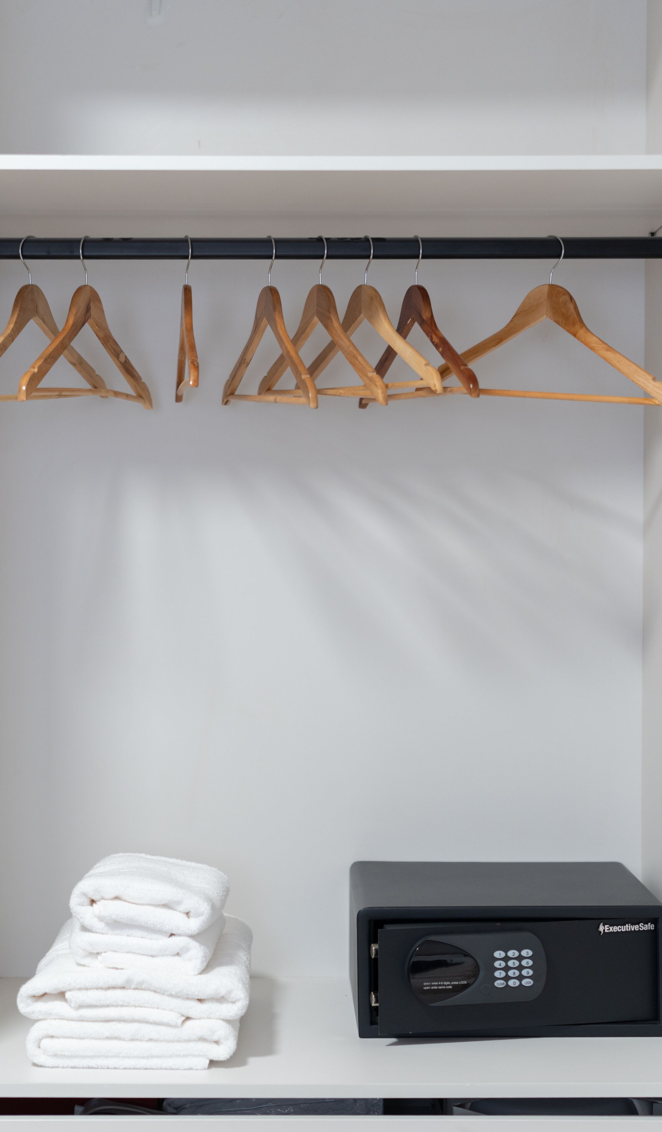 A closet with wooden hangers, folded white towels, and a black security device.