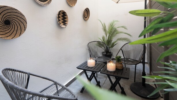 Ein kleiner Patio-Bereich mit zwei Metallstühlen, einem Tisch mit Kerzen und gewobenen Wanddekorationen.