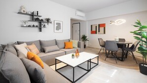 Ein modernes Wohnzimmer mit grauem Sofa, einem weißen Couchtisch und einem Essbereich mit schwarzen Stühlen und einem Tisch.