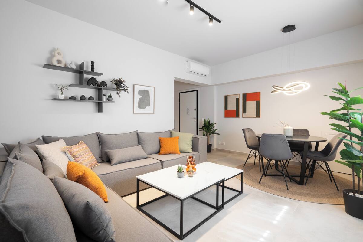 Een moderne woonkamer met een grijze bank, een witte salontafel en een eethoek met zwarte stoelen en een tafel.