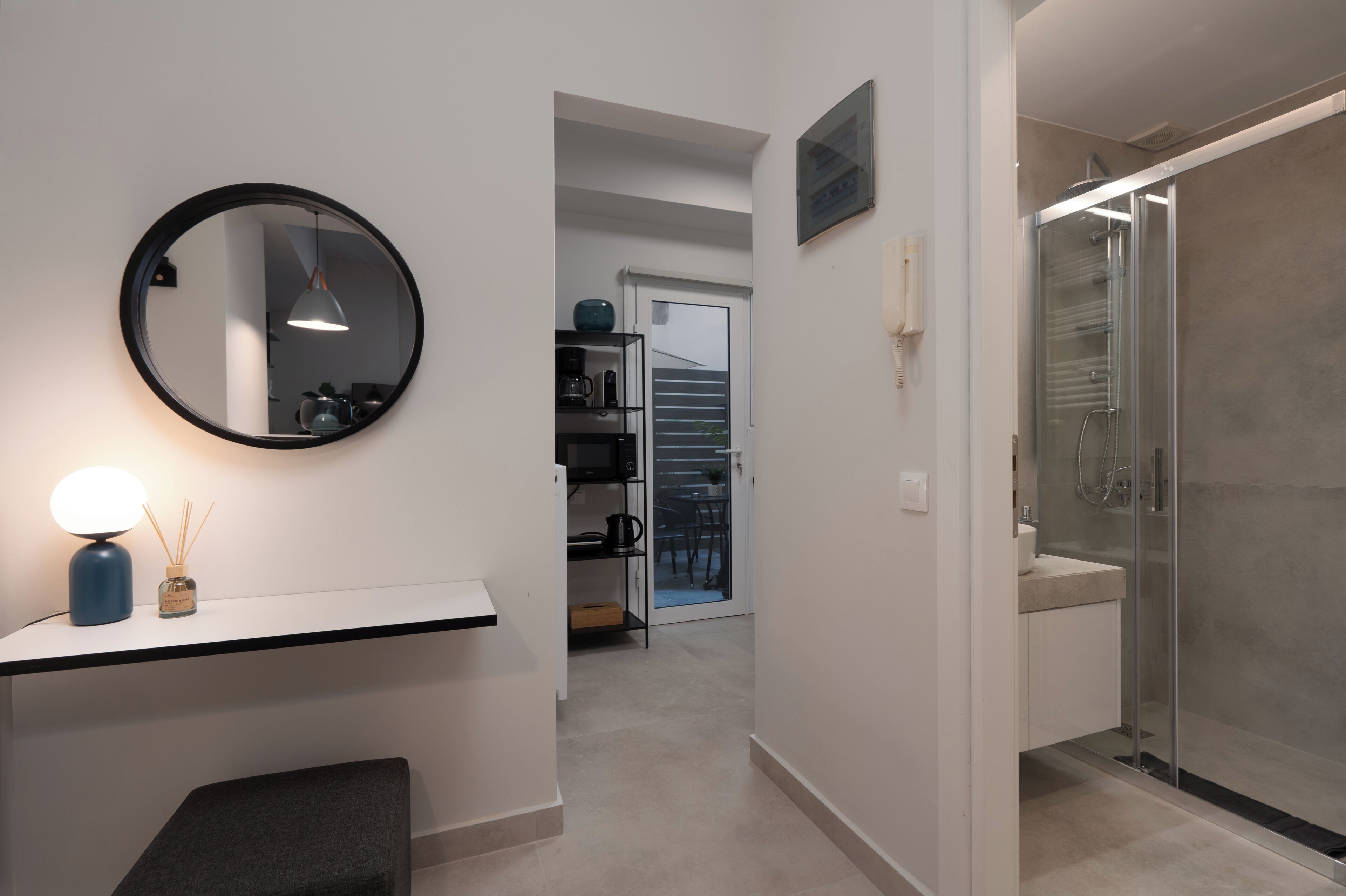 A modern bathroom with a glass shower enclosure, a round mirror, and a white countertop with a lamp.