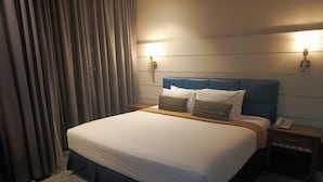 A hotel room with a large bed, a headboard, two bedside tables, a telephone, and a curtain.