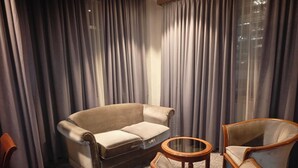 A room with a sofa and two armchairs, a small wooden side table, and a large window with curtains.