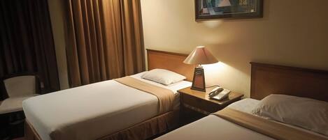 A hotel room with two beds, a nightstand with a lamp, a telephone, and a painting on the wall.