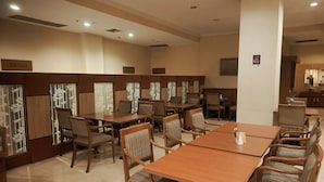 A dining area with wooden tables and chairs, recessed lighting, and decorative panels with bamboo patterns.