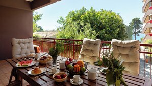Mesa de comedor dispuesta con alimentos para el desayuno, vista a zonas verdes y un balcón con barandilla.