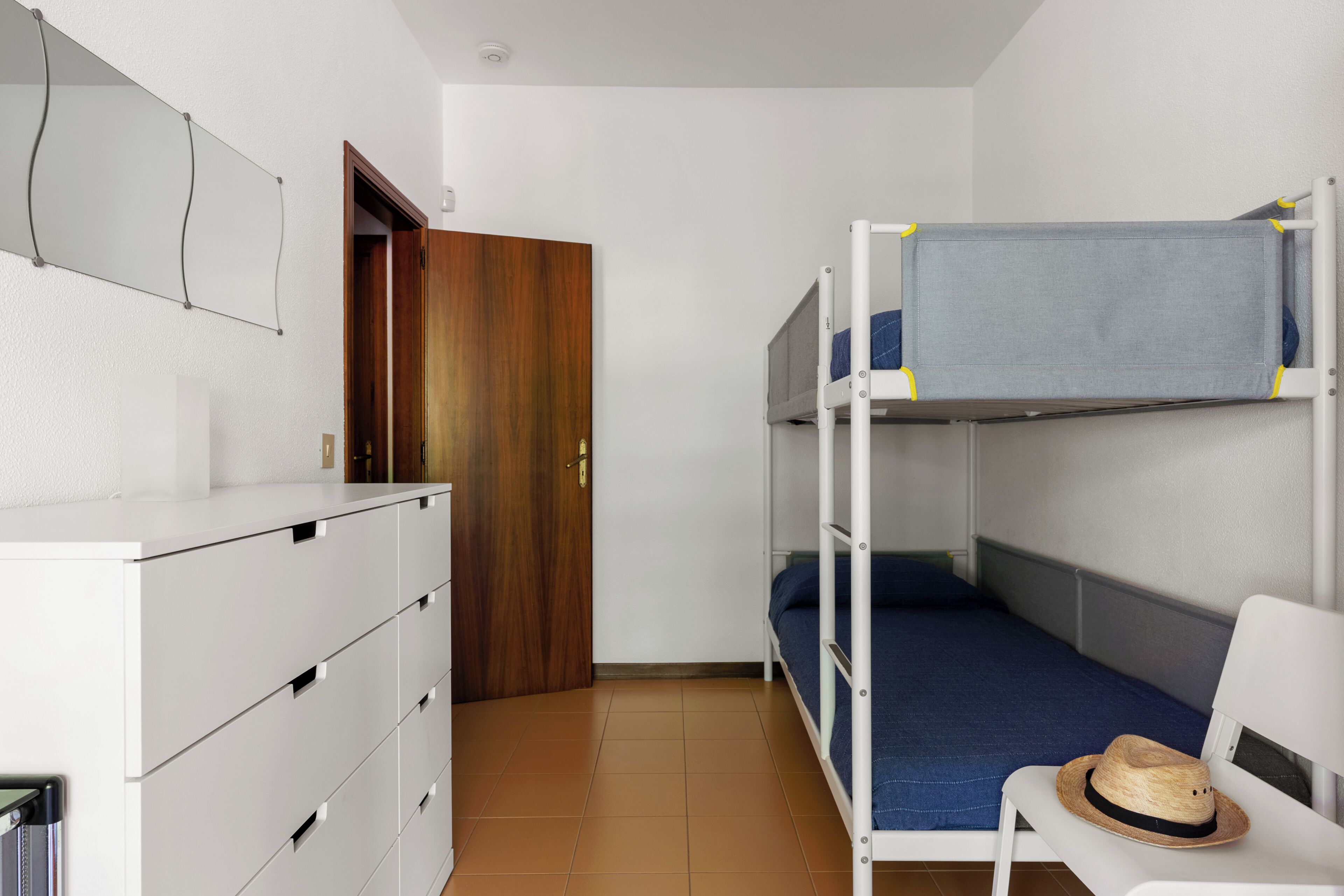 Uma cama de solteiro com um chapéu no assento, um aparador branco e uma porta de madeira.