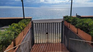 Una escalera conduce a una playa con una reja metálica, rodeada de vegetación y una vista despejada del mar.