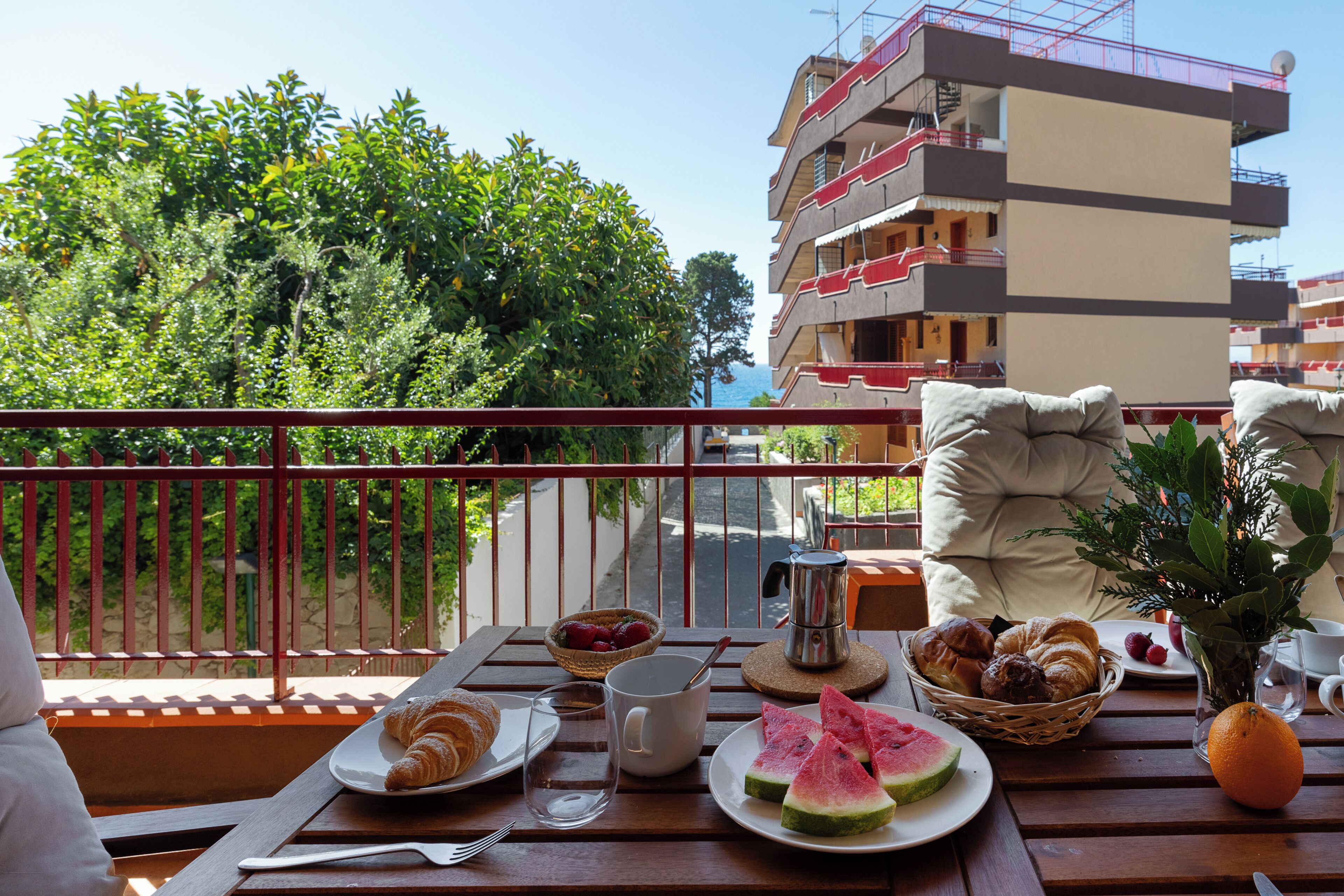 A balcony with breakfast items, a view of a building, and a potted plant.