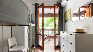Una habitación con literas, una silla, un escritorio, un armario, una ventana con vistas a la vegetación y un cuadro en la pared.