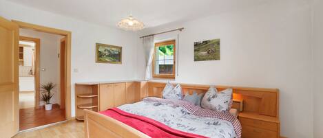 Ein Schlafzimmer mit einem hölzernen Bett, einem Nachttisch, einem Fenster mit Vorhängen und einer Topfpflanze.