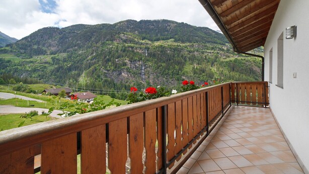 Un balcon doté d’une balustrade en bois, d’où l’on peut admirer un paysage montagneux.