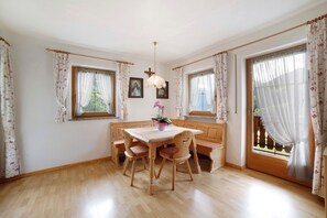 Un coin repas avec une table et des chaises en bois, un luminaire suspendu et une fenêtre avec des rideaux.