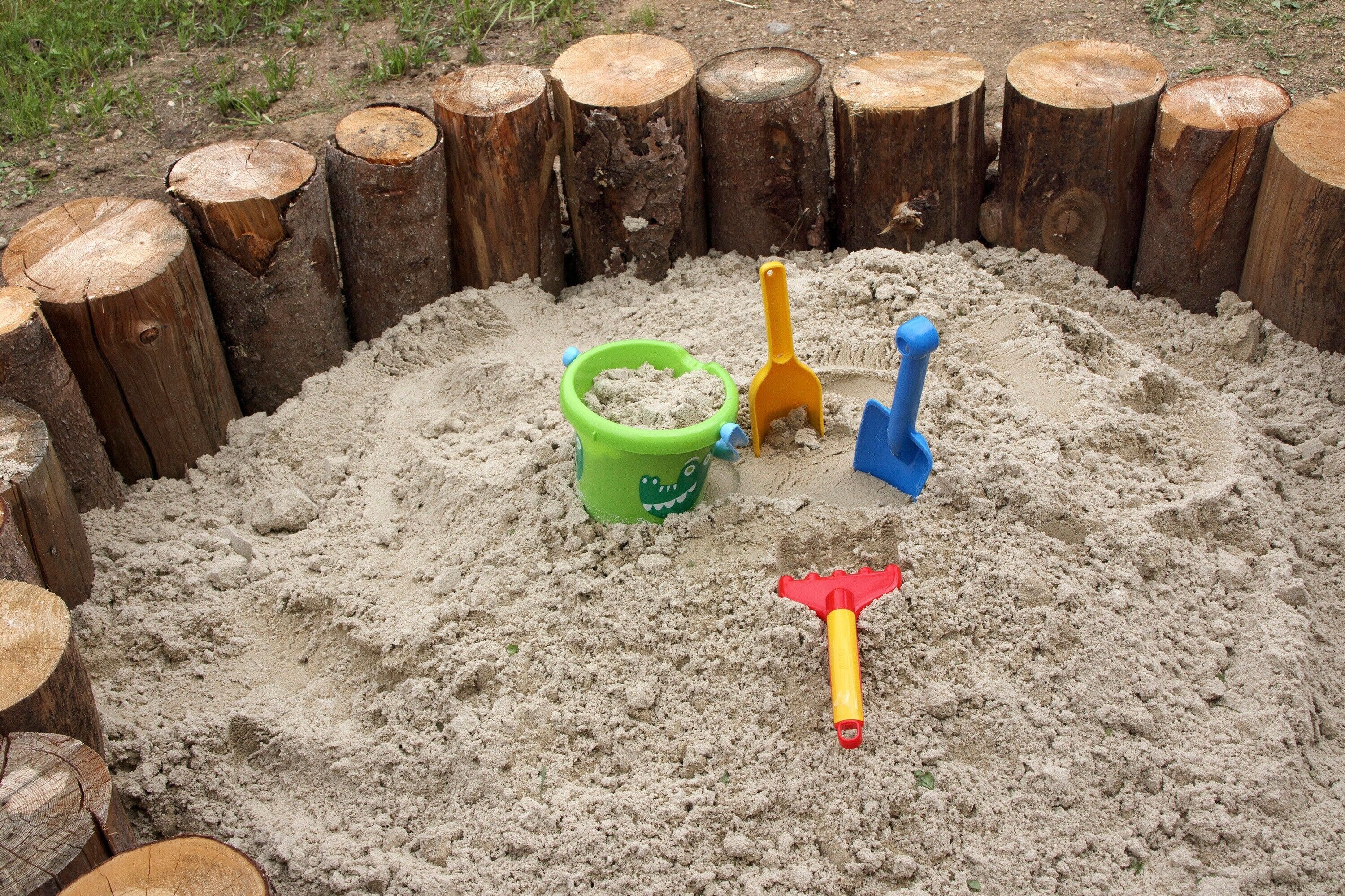 A sandbox with wooden posts and three sand toys.