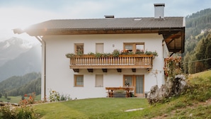 Une maison à deux étages avec un balcon, un banc en bois et un jardin.