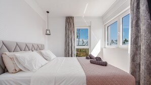 A neatly made bed with a quilted cover, a hanging pendant light, and a view of the outdoors through a window. - Villa Cvita & Mia Zadarvillas (Privlaka)