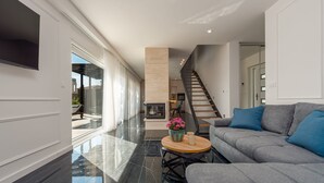 A modern living room with a grey sofa, a round wooden coffee table with a vase of flowers, a fireplace, and a staircase leading to an upper floor. - Villa Cvita & Mia Zadarvillas (Privlaka)