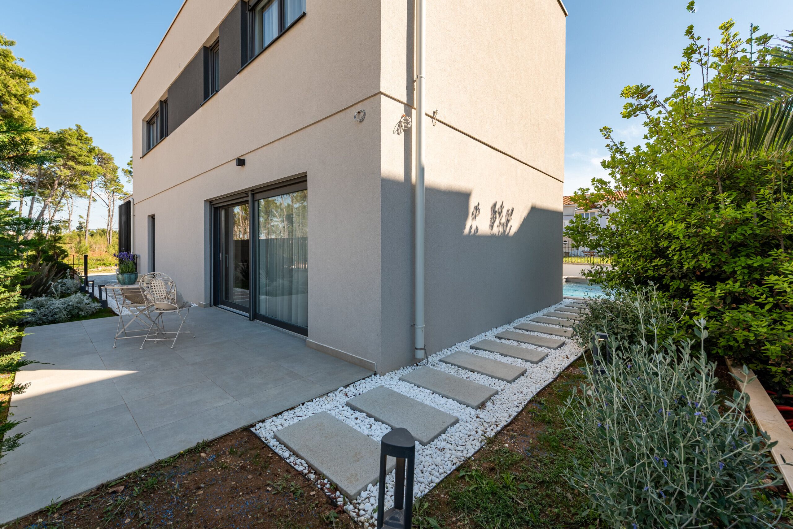 A modern building with a patio area, a seating arrangement, and a pathway leading to a pool.