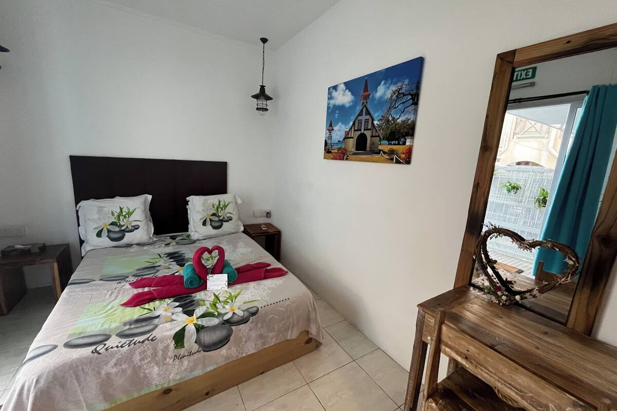 A neatly arranged hotel room with a bed, a nightstand, a wooden bench, a painting, and a mirror.