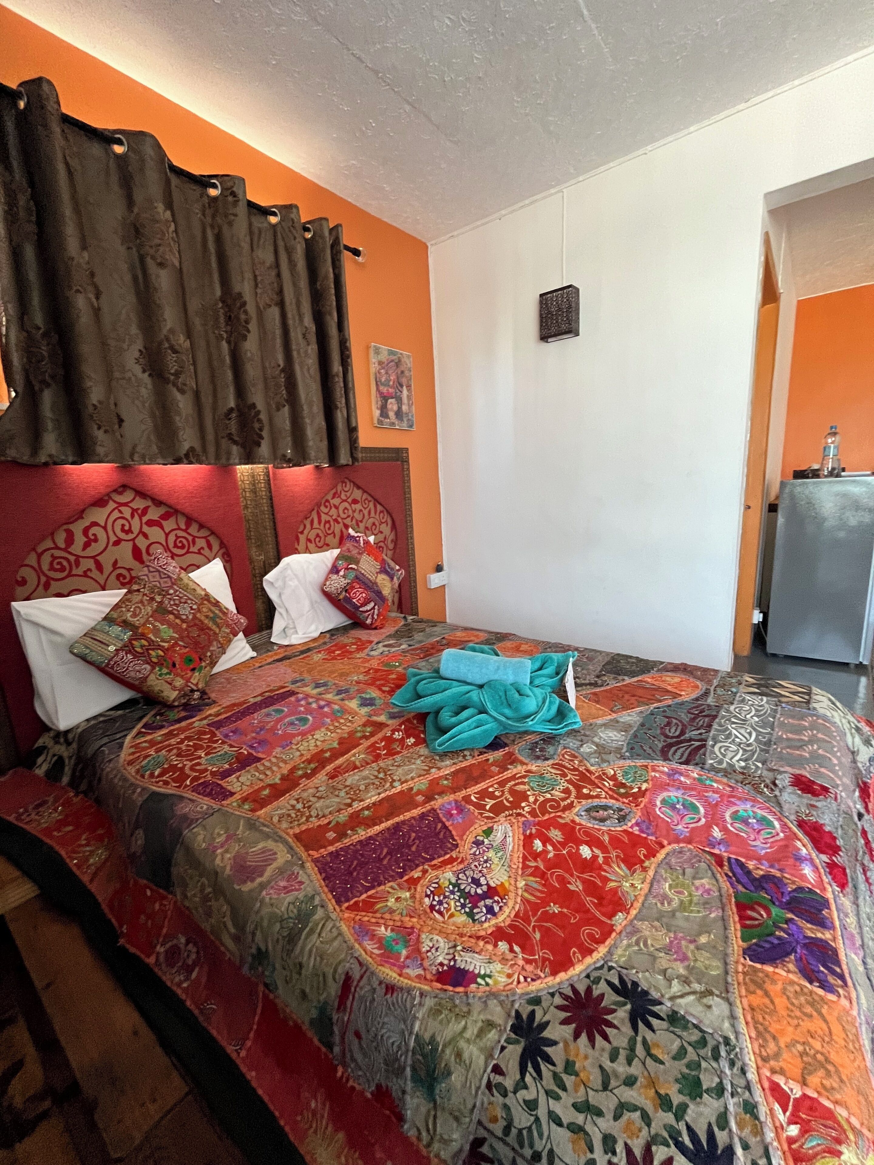A bed with a colorful quilt, a headboard, and a curtain.