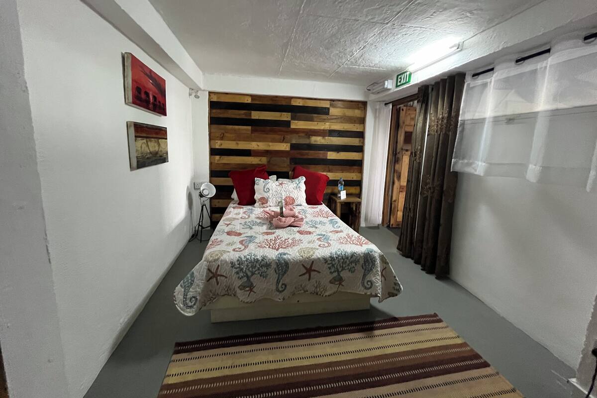 A bedroom with a wooden headboard, a bed with a floral bedspread, a striped rug, and a small table with a lamp.