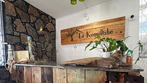Un bar rustique en bois, avec un mur en pierres en arrière-plan, une enseigne en bois portant l’inscription « La Koquillshe » et un luminaire suspendu.