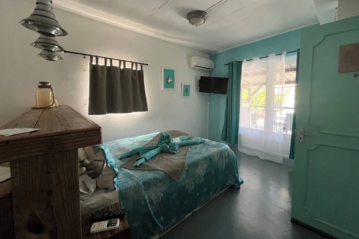 A bedroom with a bed, a desk, a lamp, a TV, and a window with curtains.
